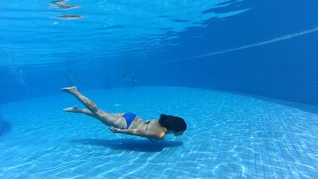 young girl swimming underwater in a blue pool under water gopro