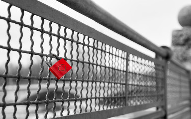 Love lock with heart shape on the bridge as symbol of infinite true love. Black and white retro vintage stock photo with selective red color effect.