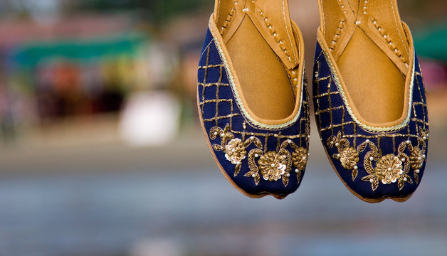 Blue colored traditional ethnic Indian jutis (women's shoes) with embroidery on a beach in north Goa, India in the evening with a blurry backgound