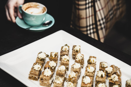 Close-up of cakes in tray, woman holding coffee cup in background