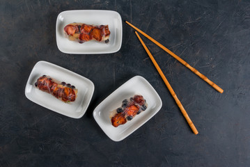 Sweet spring rolls with fruits and berries on the black stone table, next to chopsticks for sushi, top view, copy space