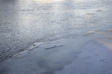 Water chipping off pieces from a large ice sheet on a lake