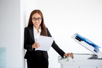 Positive young businesswoman standing at printer