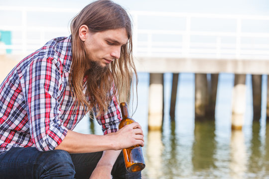 Man depressed with wine bottle sitting on beach outdoor