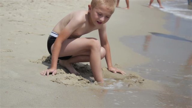 boy buries leg in the sand/Boy on the beach buries leg in the sand