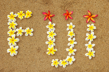 Word Fiji written on a beach with plumeria flowers