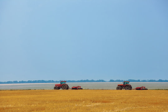 Summer day two tractors to plow plow the soil on sloping wheat. Agricultural land treatment before planting.