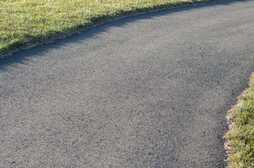 Asphalt alley among green grass fields in park in winter time