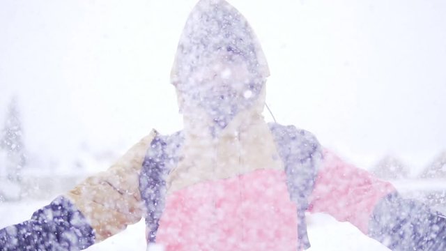 Young girl in bright winter clothes having fun outdoor in winter forest under snowflakes.