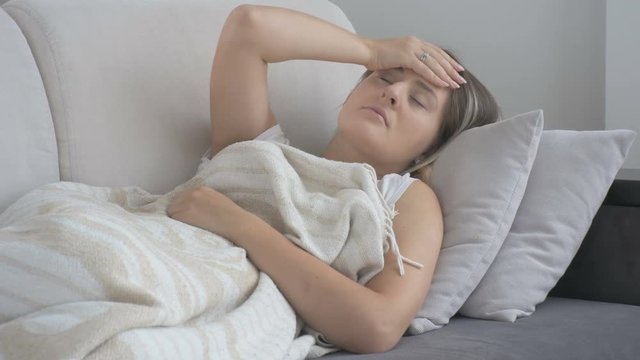 Unhappy young woman suffering from headache lying couch at living room. Footage shot in 4K