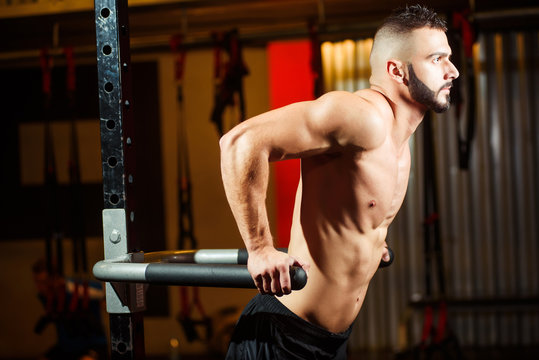 Muscular man working out in gym doing exercises on parallel bars