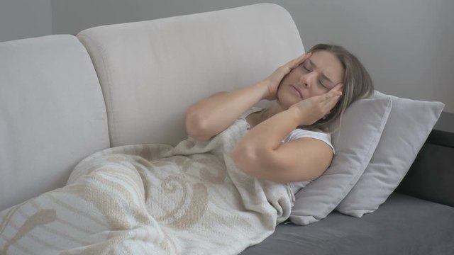 Young woman suffering from migraine lying on couch at living room. Footage shot in 4K
