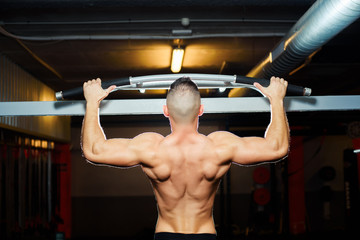 Athlete muscular fit man pulling up on horizontal bar in a gym