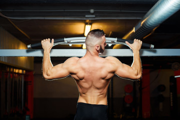 Fototapeta na wymiar Athlete muscular fit man pulling up on horizontal bar in a gym