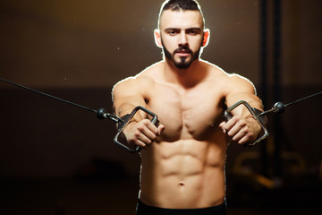 Fototapeta na wymiar Young athletic tired man with beard pumping up muscles on crosso