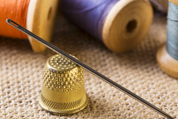 Sewing concept. Needle with thimble close up near thread spools on canvas background