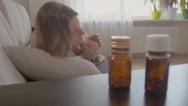 Young woman felling sick caughing in bed and taking pills from bedside table