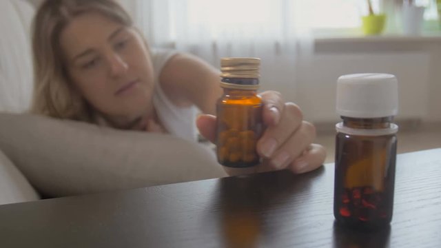 Young woman feeling sick taking container with medicines from bedside table