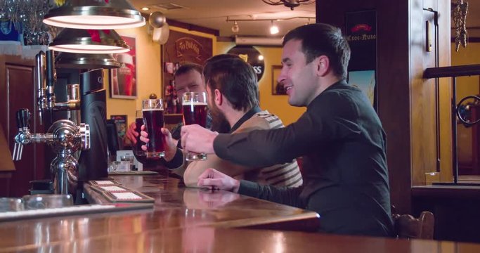 Friends group talks and drinks beer at pub bar 4k close-up video. Men doing toast, cheers and having fun, drinks brown lager or ale from glasses