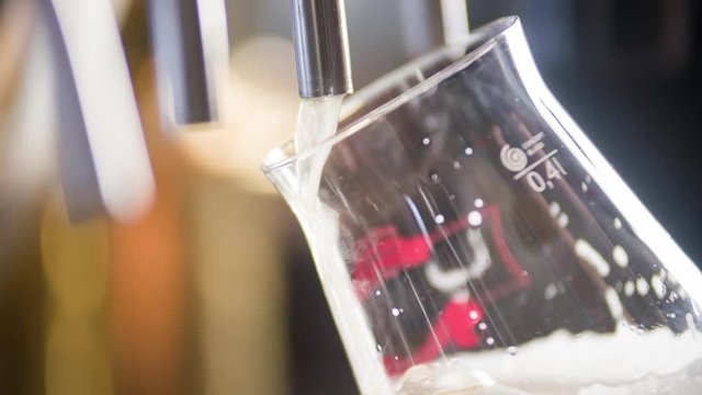 Craft beer pouring to glass in pub bar HD slow-motion close-up video. Lager, ale or dunkel falls from a cask to stemware