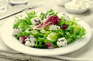 Green salad with spinach, frisee, arugula, radicchio, feta cheese and black sesame seed on blue wooden background