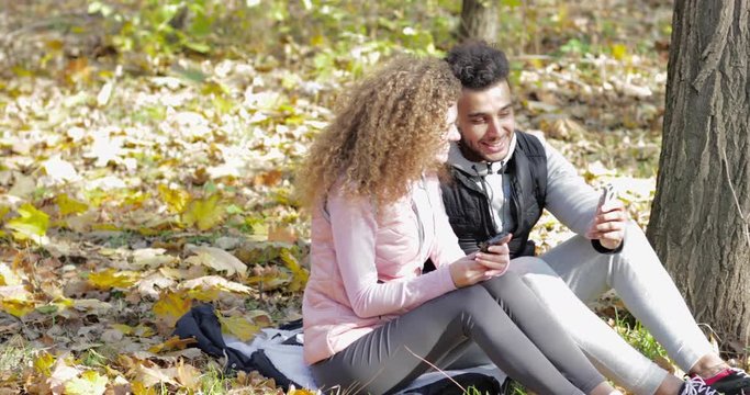 Young Couple Group Sit On Ground In Forest Using Smart Phone Outdoor Autumn Park Slow Motion 60 Fps