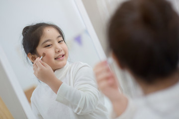 Obraz na płótnie Canvas Pretty Asian child doing make up front of the mirror