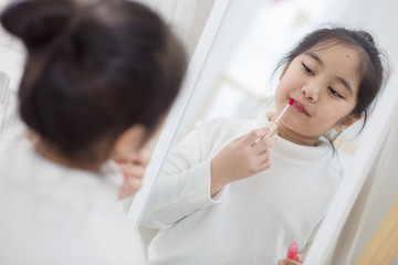 Obraz na płótnie Canvas Pretty Asian child doing make up front of the mirror