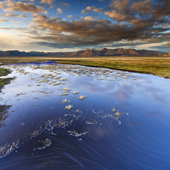 Wetlands in California at Sunset. River leads off into the distance towards mountain range with colorful reflections in water.