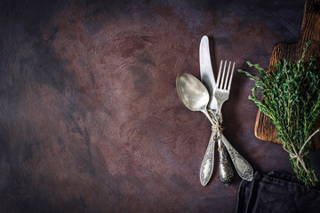 Vintage silverware on a dark textile and bunch of fresh thyme on dark rusty background. Top view,...