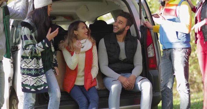 Young Friends Sitting In Car Trunk Outdoors In Autumn Park, Mix Race People Group Happy Smile Talking Slow Motion 60