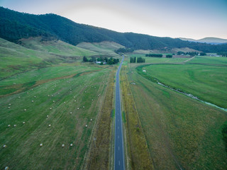 Aerial view of Omeo highway among green fields and hay bales in Mitta Mitta Valley, Victoria, Australia