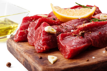 Pieces of meat with garlic, lemon and rosemary on wooden board isolated. Raw beef.
