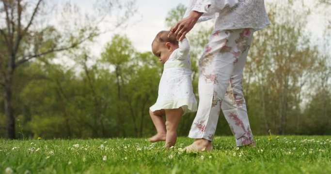 On a sunny day a baby takes its first steps on its own and in the hands of the newborn is a pinwheel, smiling and happy baby falls but rises again.