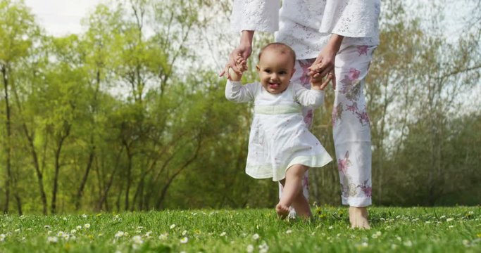 On a sunny day a baby takes its first steps on its own and in the hands of the newborn is a pinwheel, smiling and happy baby falls but rises again.