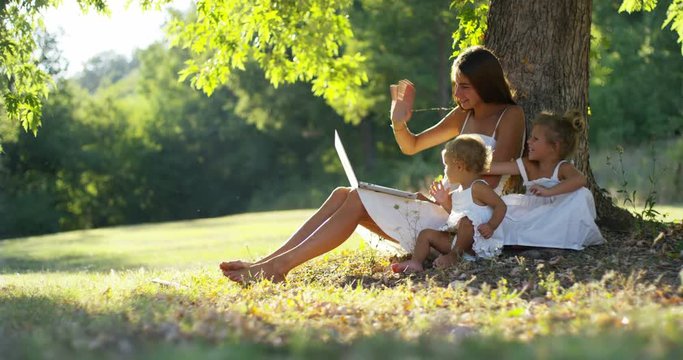 mother with little girls dressed in a vintage lawnsitting close to a tree in sunset happy little girl in nature. video calls with your tablet relatives and greet family