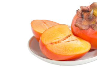 Fragment of whole and cut of persimmons on saucer closeup