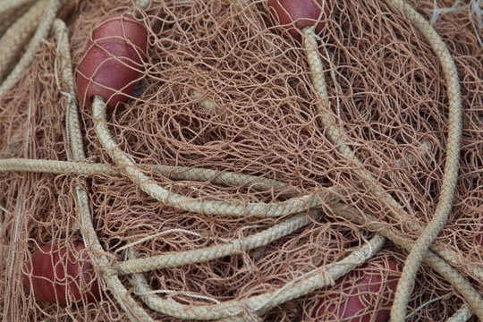 A texture image of a folded large fishing net with red floats and thick ropes