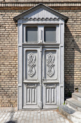 Old vintage wooden white door with floral patterns on the brick wall background. Grodno, Belarus.