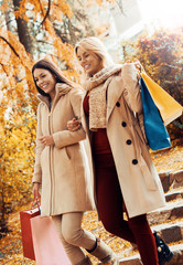 Two beautiful girls in the autumn park after shopping. Consumeri