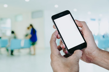 Man hands holding smart phone with blank screen in hospital waiting room, light bokeh background.