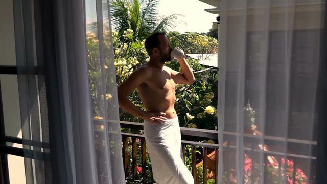 Young man drinking coffee in towel standing on terrace, super slow motion 240fps
