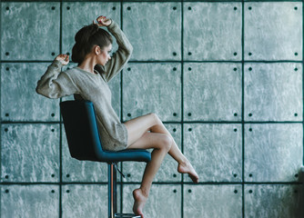 Beautiful girl sitting on a chair. A woman dressed in a soft knit sweater. Photo in a quiet and cozy style. The model have fashionable and stylish hairstyle and make-up.