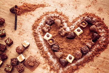 Delicious chocolate candies, truffles in a cocoa heart shape on the wooden background.
