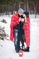 Loving couple in the winter under a blanket with a cup of hot coffee or tea, it's snowing