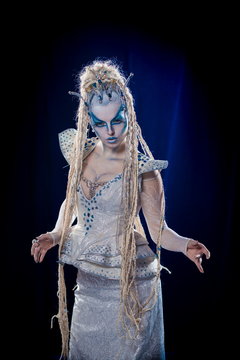emotional actress woman in makeup and costume queen of elves or snow queen on blue-black background