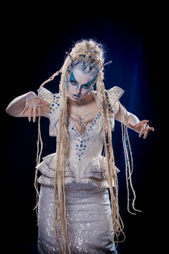 emotional actress woman in makeup and costume queen of elves or snow queen on blue-black background