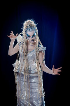 emotional actress woman in makeup and costume queen of elves or snow queen on blue-black background