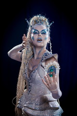 emotional actress woman in makeup and costume queen of elves or snow queen on blue-black background