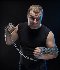 Actor Brutal man with a chain in his hands on a black background.